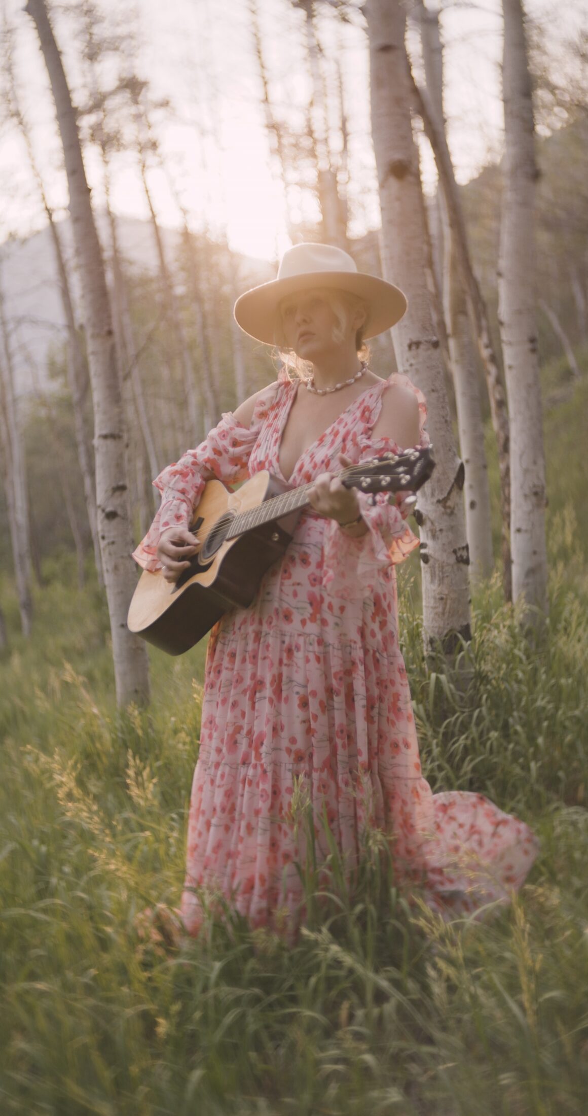 Clar singing and playing acoustic guitar among aspen trees
