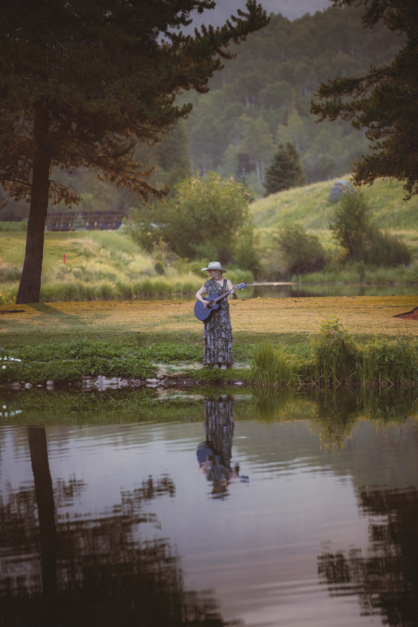 Clar performing with acoustic guitar beside water in the Vail Valley