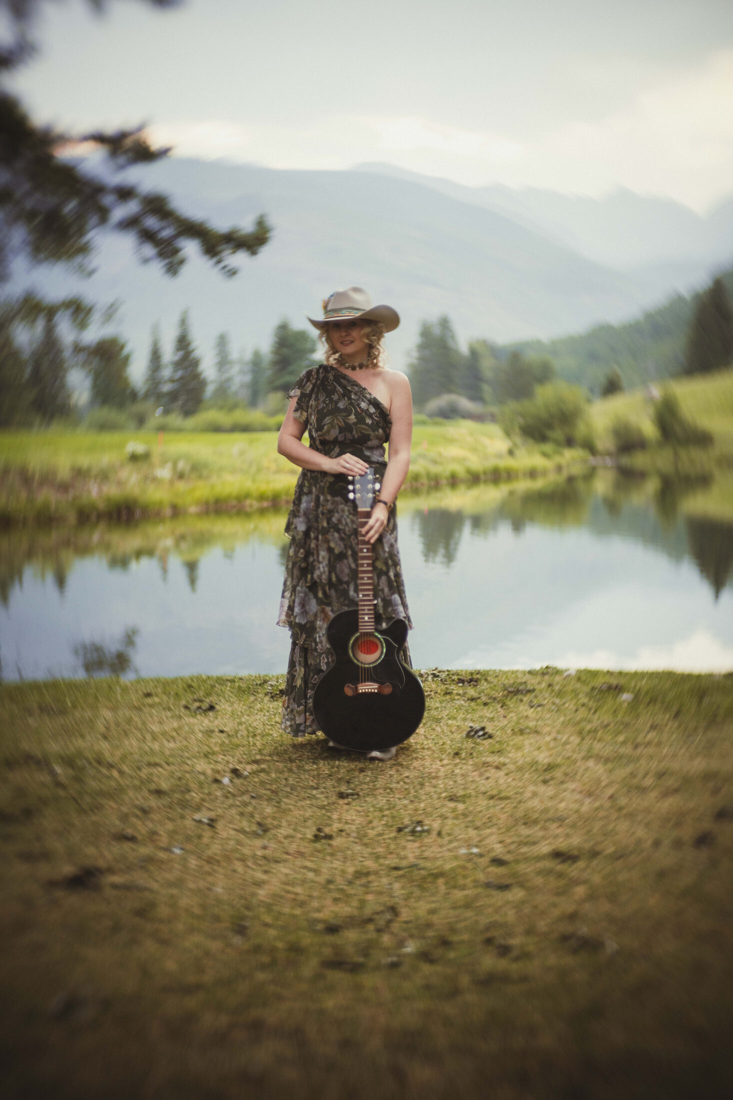 Clar standing with guitar in front of Vail Valley mountains